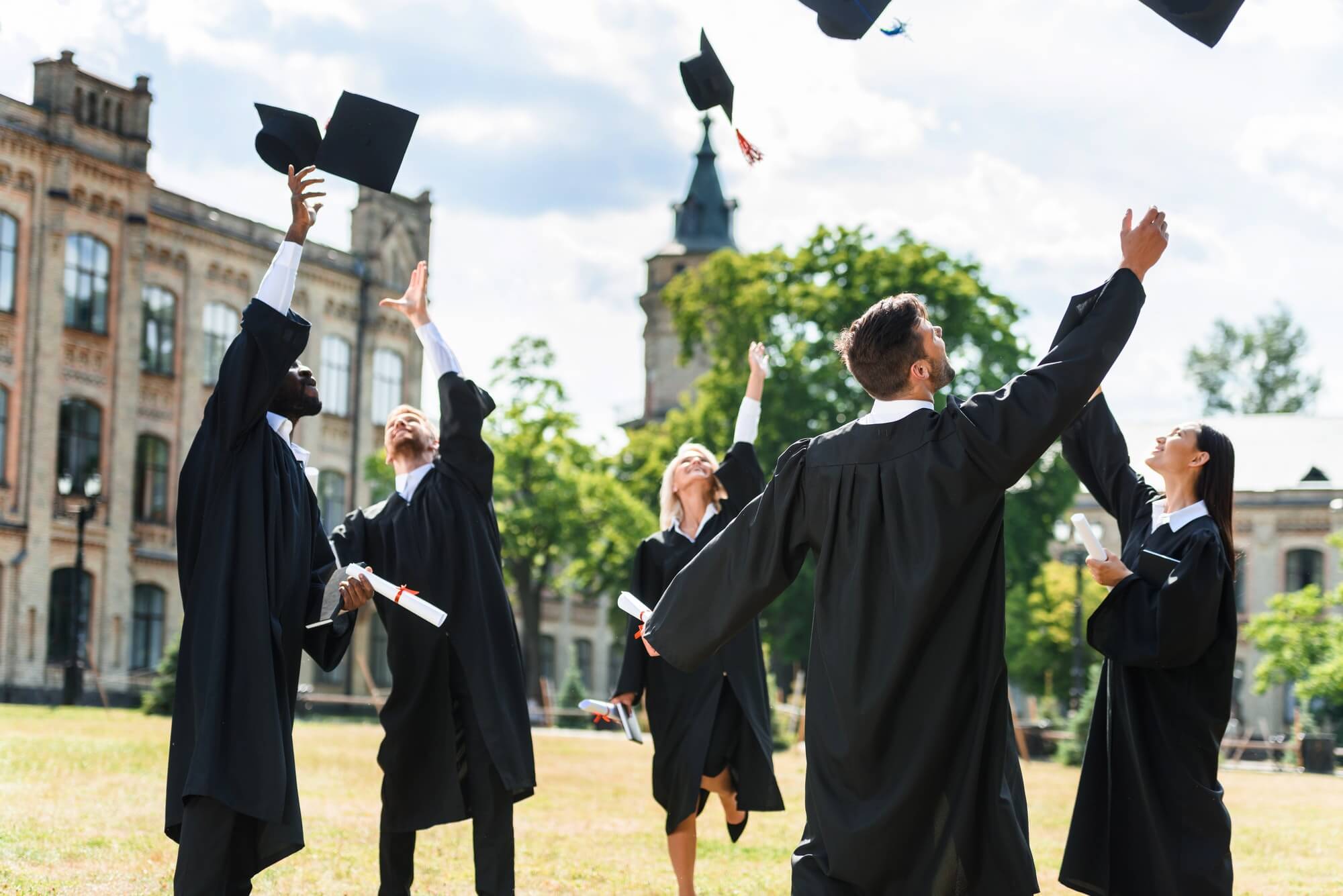 young graduated students throwing up graduation caps in university garden